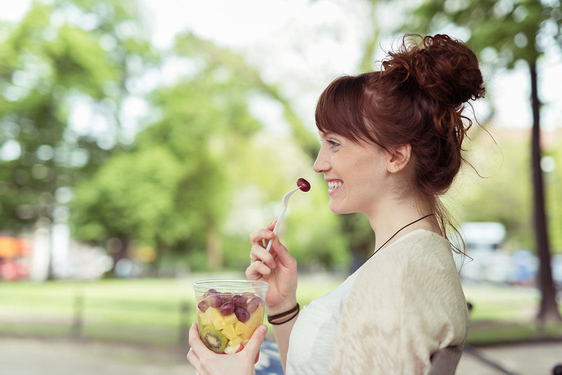 Woman eating fruit cup with compostable fork in park